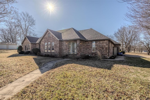 view of front of home featuring a shingled roof, a front lawn, and brick siding