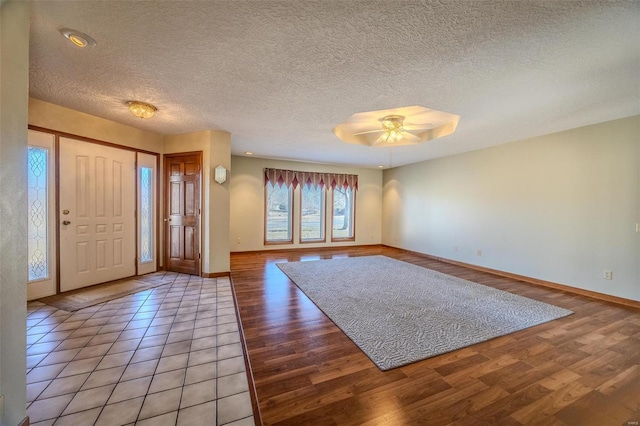 foyer entrance with a ceiling fan, baseboards, a textured ceiling, and light wood finished floors