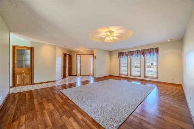 unfurnished living room featuring a ceiling fan, a textured ceiling, baseboards, and wood finished floors