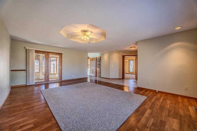 empty room with ceiling fan, a textured ceiling, wood finished floors, and baseboards