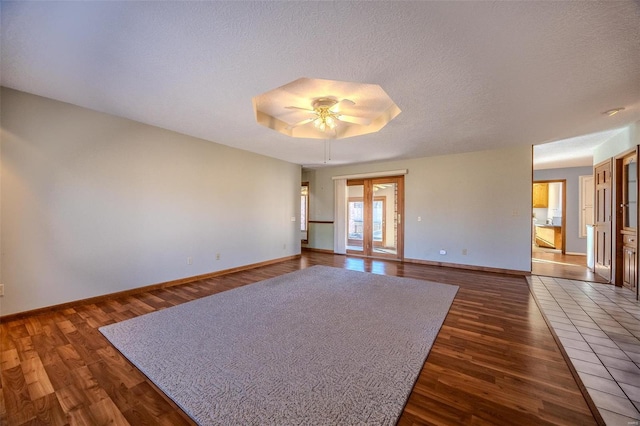 spare room featuring baseboards, wood finished floors, a tray ceiling, a textured ceiling, and french doors