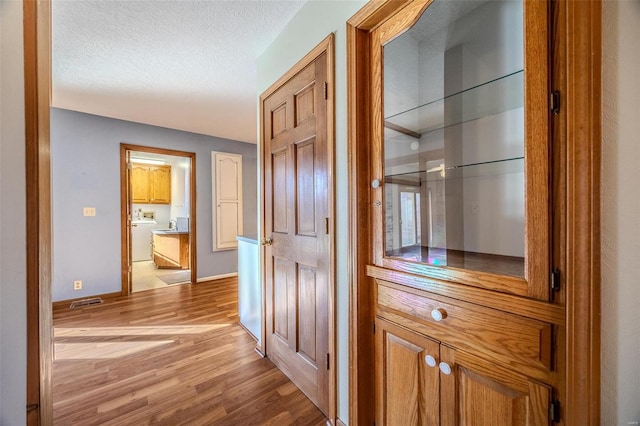 hallway with visible vents, a textured ceiling, light wood-type flooring, washer and dryer, and baseboards