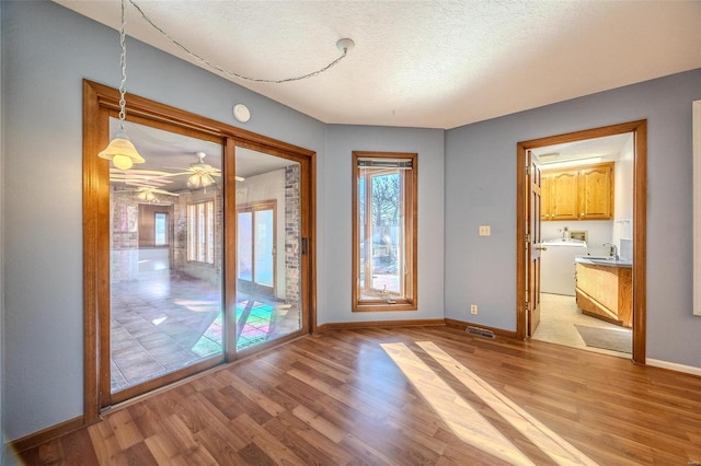 doorway to outside with a textured ceiling, a sink, light wood-style flooring, and baseboards