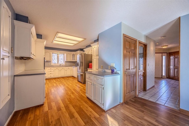 kitchen with white cabinets, a sink, light wood-style flooring, and stainless steel fridge with ice dispenser