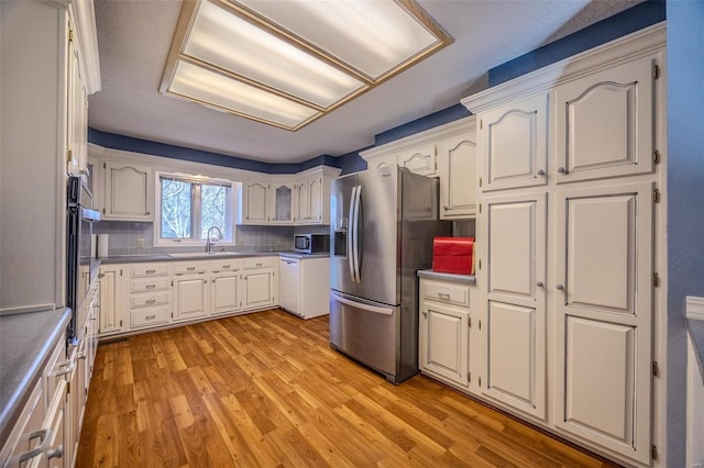 kitchen featuring light wood-style flooring, decorative backsplash, stainless steel appliances, and a sink