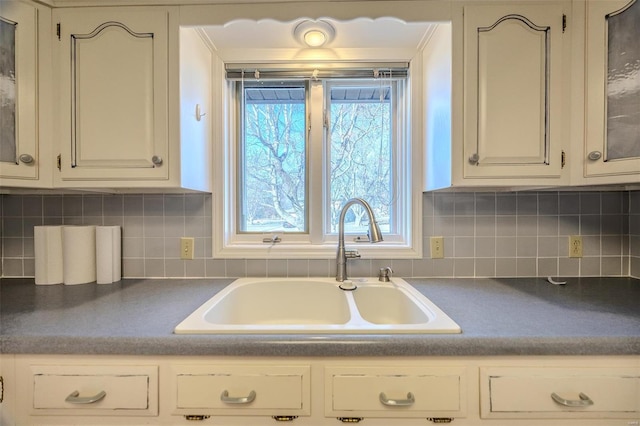 kitchen featuring dark countertops, glass insert cabinets, decorative backsplash, and a sink