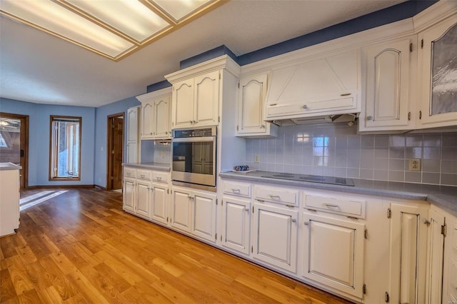 kitchen featuring tasteful backsplash, range hood, black electric cooktop, light wood-style floors, and stainless steel oven