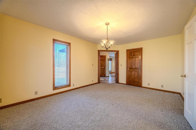 empty room featuring carpet, a textured ceiling, a chandelier, and baseboards