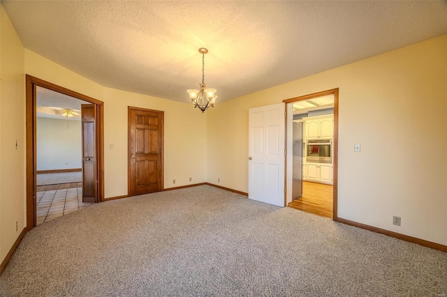 interior space with a notable chandelier, a textured ceiling, baseboards, and light colored carpet