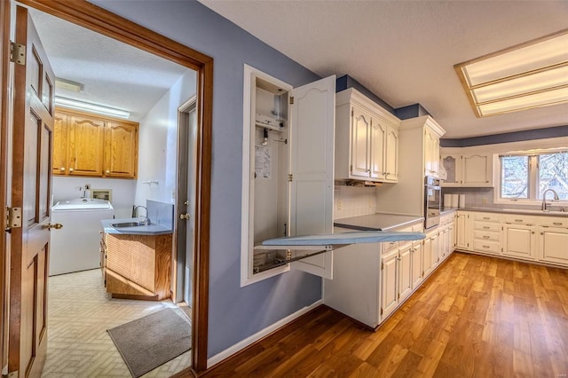 kitchen with light wood-style floors, baseboards, washer / clothes dryer, and a sink