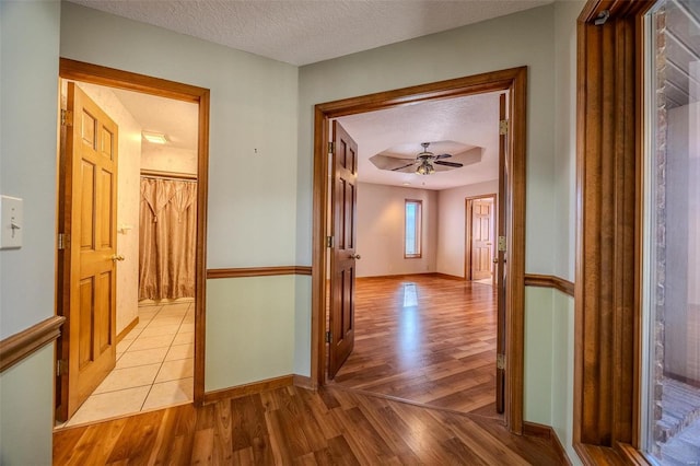 hallway featuring baseboards, a textured ceiling, and wood finished floors