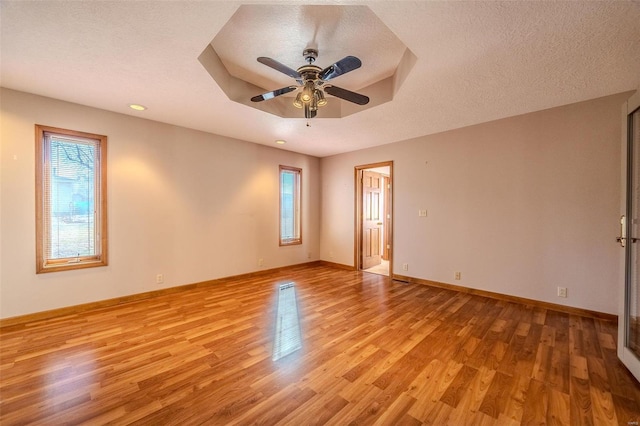 unfurnished room with light wood finished floors, baseboards, a tray ceiling, and a textured ceiling