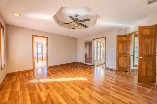 empty room featuring baseboards, a raised ceiling, visible vents, and light wood-style floors