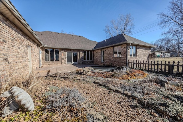 back of house with a shingled roof, brick siding, fence, and a patio