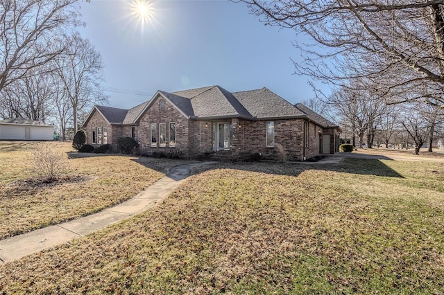 view of front of house with an outbuilding, a garage, brick siding, roof with shingles, and a front yard