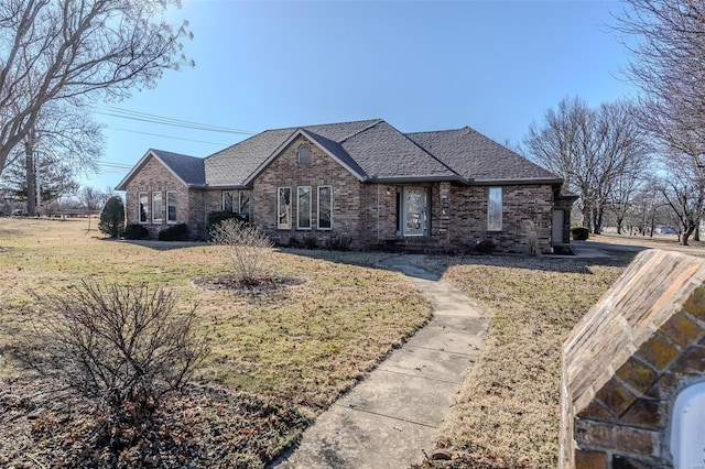 view of front of home with roof with shingles, brick siding, and a front lawn