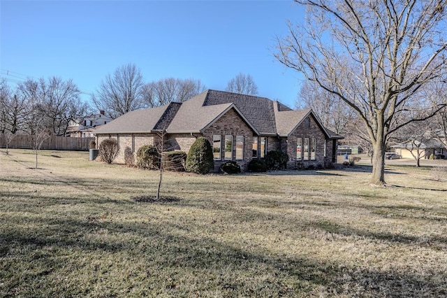 view of front of home with a shingled roof, fence, a front lawn, and brick siding