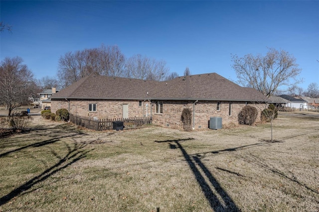 rear view of property with a shingled roof, brick siding, a lawn, and central air condition unit