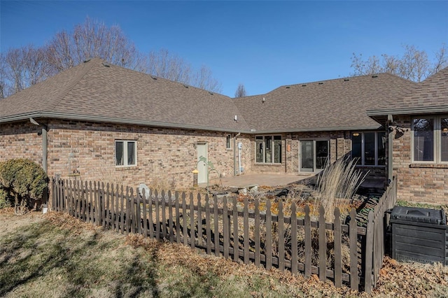 back of house featuring brick siding, fence, and roof with shingles