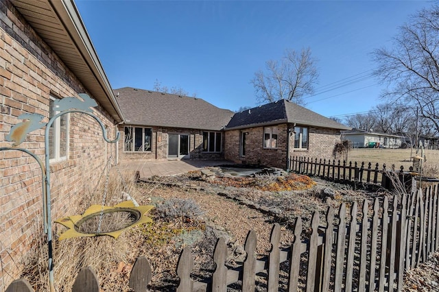 back of property with fence private yard, roof with shingles, a patio, and brick siding