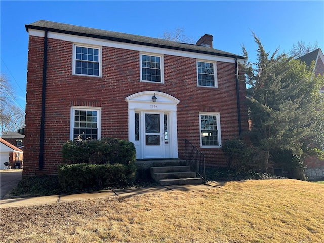 colonial-style house with entry steps, a front lawn, a chimney, and brick siding