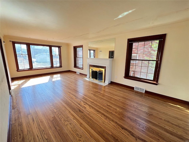 unfurnished living room featuring a fireplace with flush hearth, visible vents, baseboards, and wood finished floors