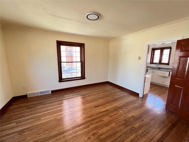 spare room with dark wood-style floors, visible vents, a sink, and crown molding