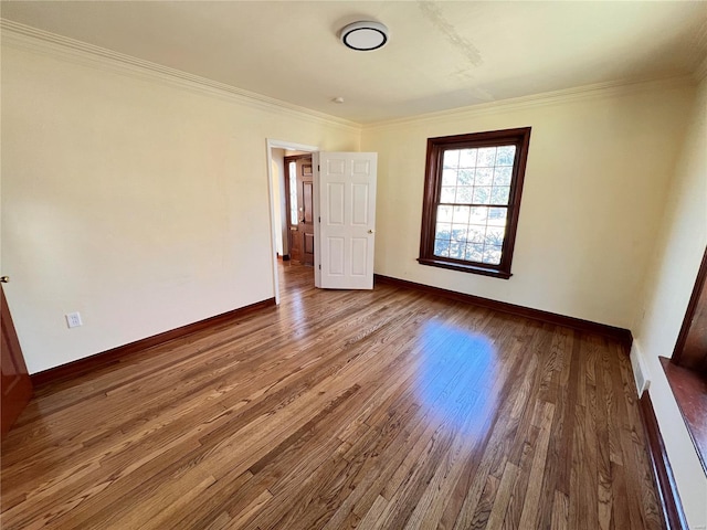 empty room featuring baseboards, visible vents, ornamental molding, and wood finished floors