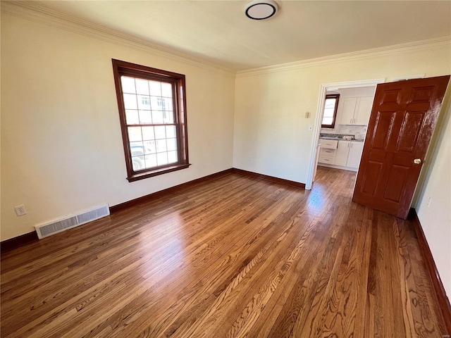 empty room with ornamental molding, wood finished floors, visible vents, and baseboards