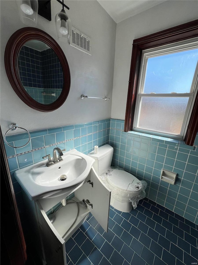 bathroom featuring toilet, a sink, visible vents, tile walls, and tile patterned floors