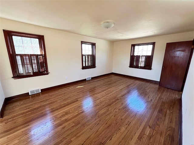 spare room featuring dark wood-style flooring, visible vents, and baseboards