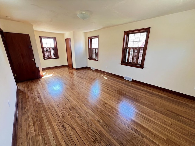 unfurnished room featuring visible vents, baseboards, and wood finished floors