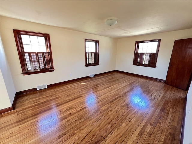 empty room with a healthy amount of sunlight, baseboards, visible vents, and wood finished floors