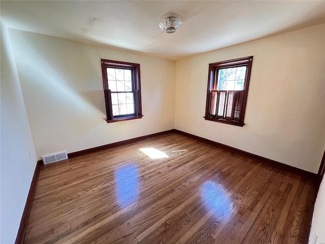 spare room featuring dark wood-style flooring, visible vents, and baseboards