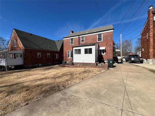 back of property featuring brick siding, a chimney, and a lawn