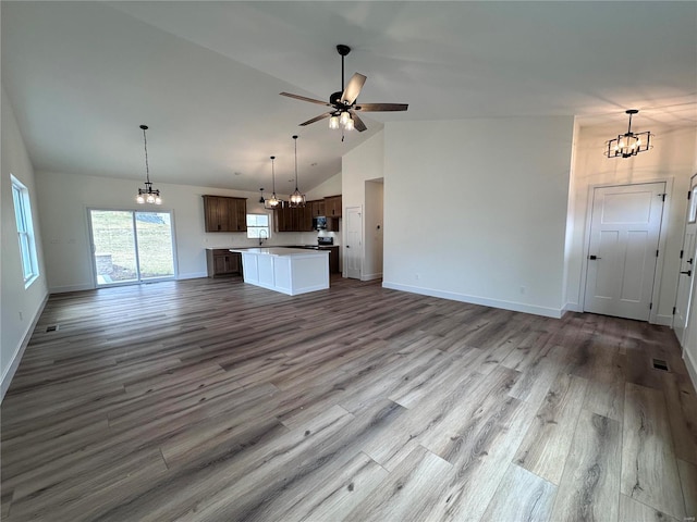 unfurnished living room featuring baseboards, light wood-style floors, high vaulted ceiling, a sink, and ceiling fan with notable chandelier