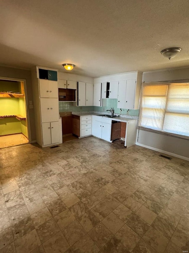 kitchen featuring baseboards, visible vents, white cabinets, light countertops, and a sink