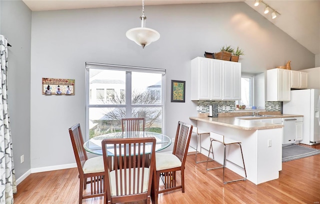 dining space featuring high vaulted ceiling, rail lighting, light wood-style flooring, and baseboards