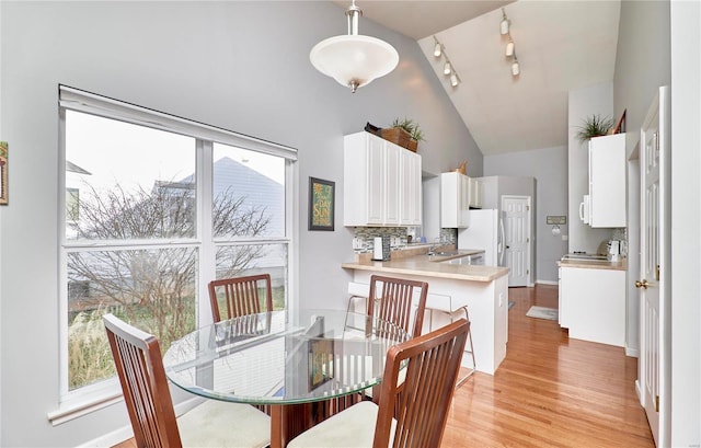 dining space with high vaulted ceiling, light wood-type flooring, and a healthy amount of sunlight