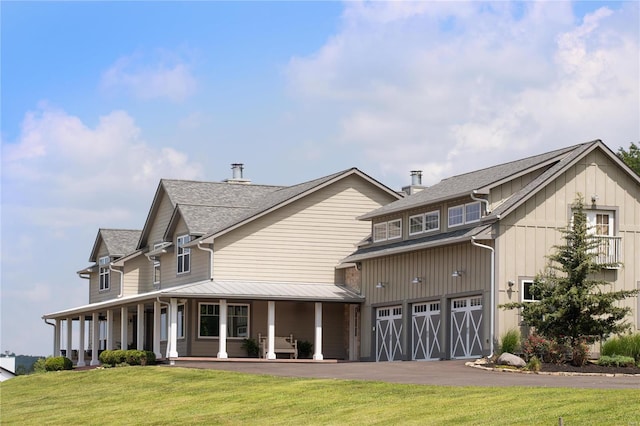 rear view of property featuring covered porch, a lawn, an attached garage, board and batten siding, and driveway