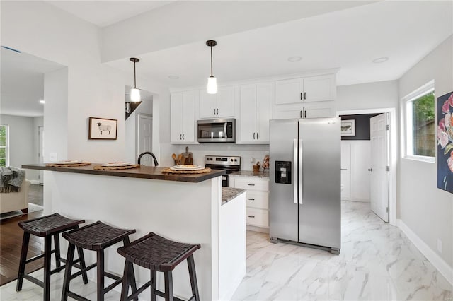 kitchen with stainless steel appliances, a wealth of natural light, marble finish floor, and a breakfast bar