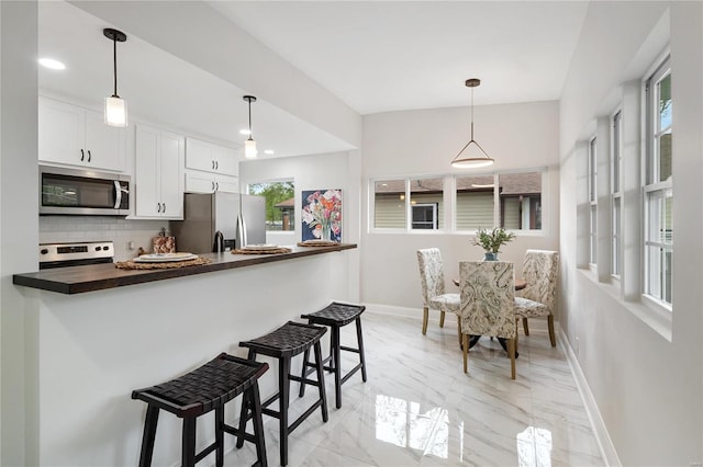 kitchen with marble finish floor, decorative backsplash, appliances with stainless steel finishes, white cabinetry, and baseboards