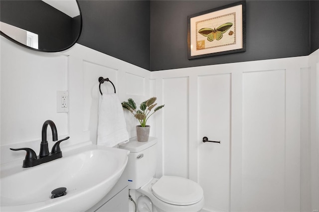 half bathroom with wainscoting, a sink, toilet, and a decorative wall