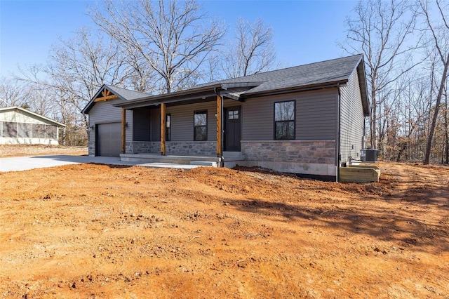 view of front facade with central air condition unit, covered porch, concrete driveway, a garage, and stone siding