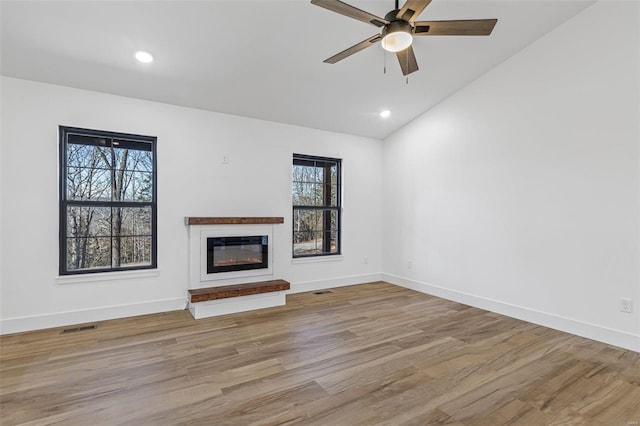 unfurnished living room featuring baseboards, visible vents, a glass covered fireplace, lofted ceiling, and wood finished floors