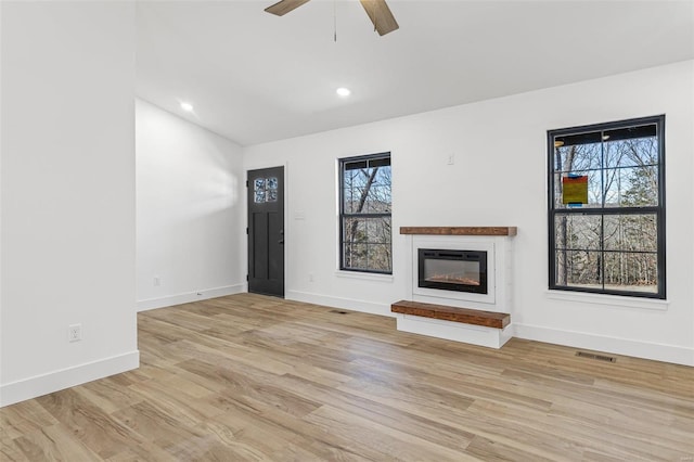 unfurnished living room featuring light wood-style floors, a glass covered fireplace, visible vents, and baseboards