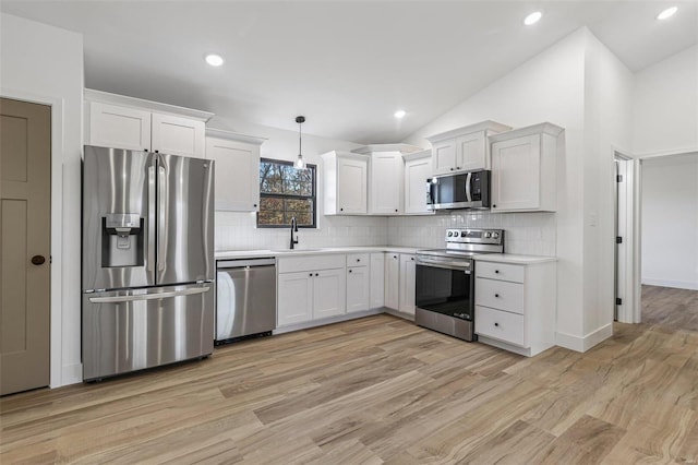 kitchen with stainless steel appliances, a sink, vaulted ceiling, light countertops, and light wood-type flooring