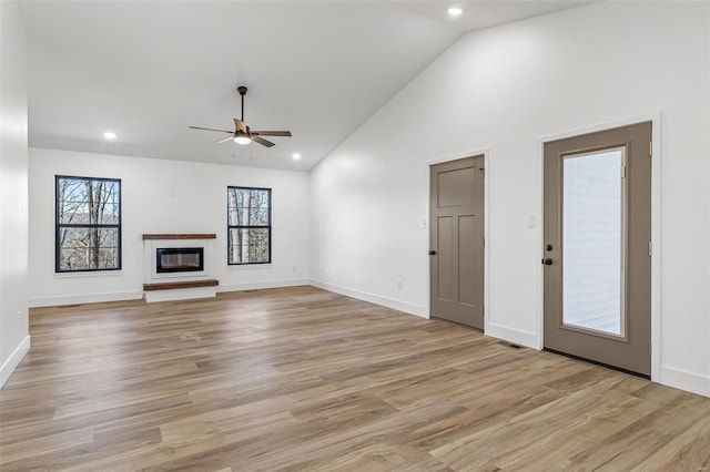 unfurnished living room featuring light wood finished floors, baseboards, a ceiling fan, a glass covered fireplace, and high vaulted ceiling