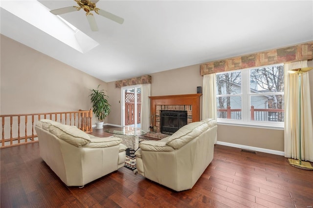 living area featuring a fireplace, visible vents, dark wood-type flooring, lofted ceiling with skylight, and baseboards