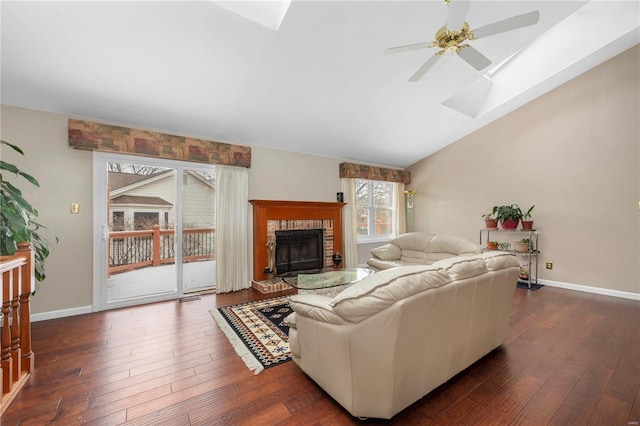 living room with dark wood-type flooring, lofted ceiling with skylight, a brick fireplace, and baseboards